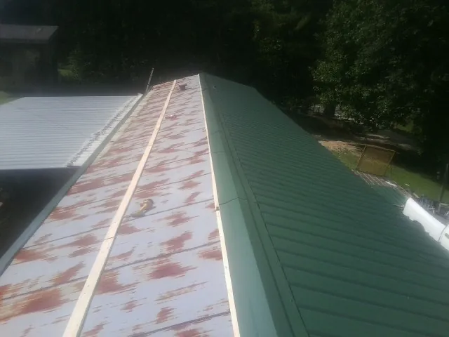 Old rusted panels beside newly installed green metal roofing — Wind Damage Roof Repair by Roofing Brothers in Allendale