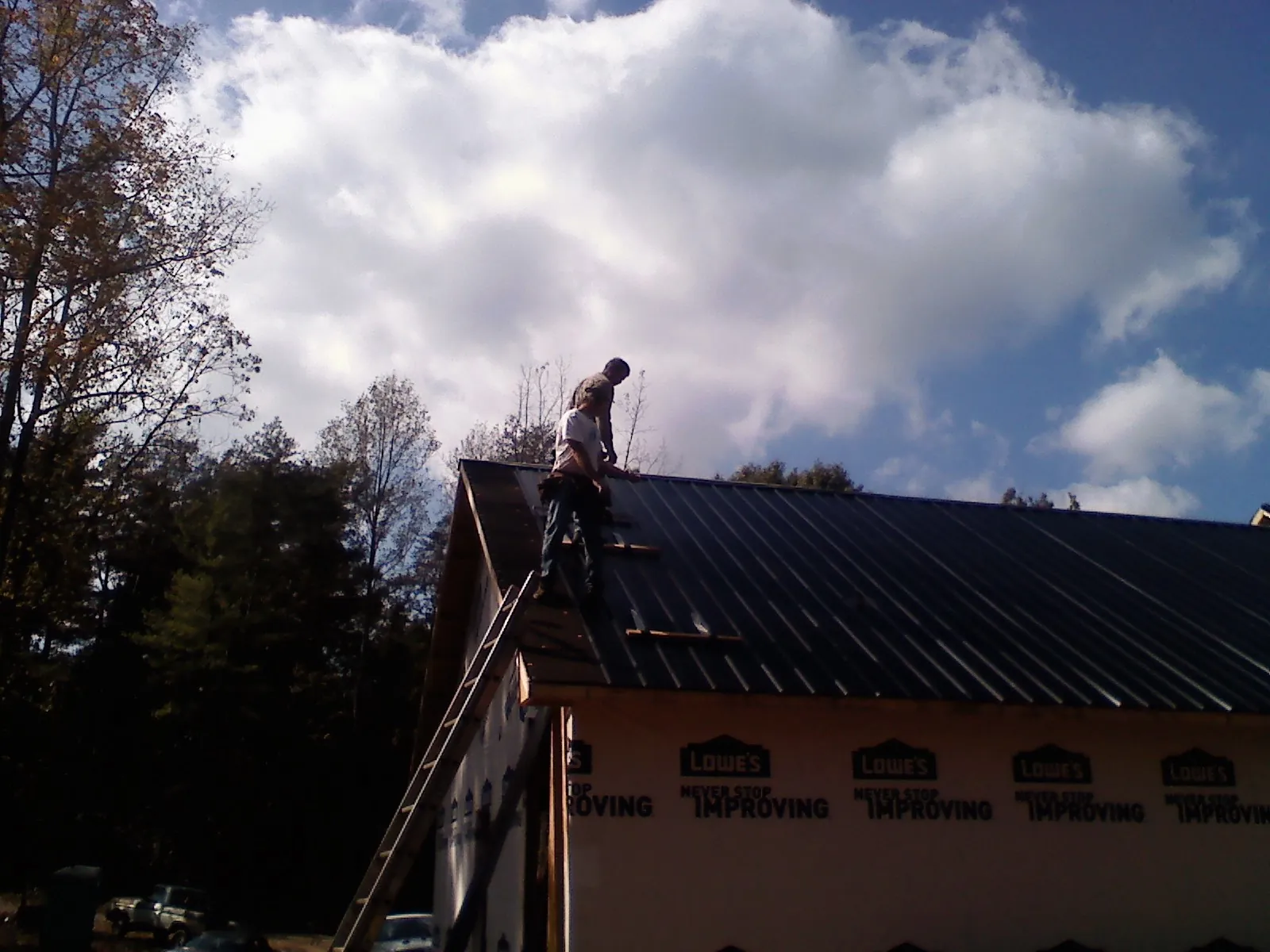 Roofer fastening dark metal panels high against a cloudy sky, from a Roof Inspection job in Allendale